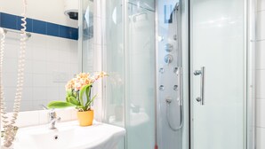 Un baño moderno con cabina de ducha de vidrio, un lavamanos blanco con un florero amarillo y una pared con azulejos azules y blancos.