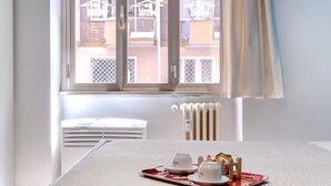 Habitación de hotel con cama, ventana con vista a edificios, radiador y una mesa con una bandeja de objetos.