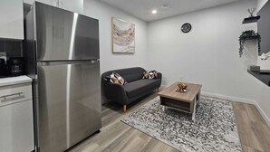 A modern kitchen with a stainless steel refrigerator, a dark sofa, a wooden coffee table, and a patterned rug. - Parkside Basement Suite/Netflix, Amazon Prime & Disney  (Edmonton)