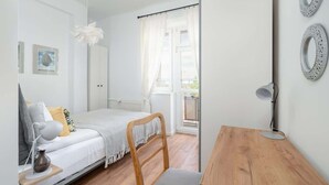 Quarto com cama, cadeira, escrivaninha e janela com cortinas.