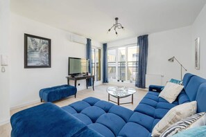 Un salon moderne avec un canapé bleu, une table basse en verre, un téléviseur et un tableau accroché au mur.