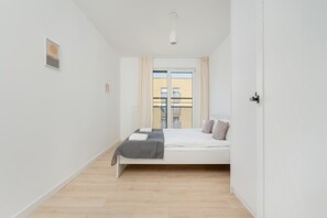 Une chambre à coucher au style minimaliste, avec un lit, une fenêtre avec des rideaux et une vue sur les bâtiments environnants.