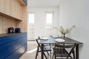 Une cuisine moderne avec des meubles bleus, une table à manger dressée pour deux personnes et un vase rempli de fleurs.