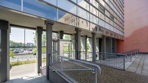 A modern building with a glass facade, outdoor stairs, and a parking lot in the background.