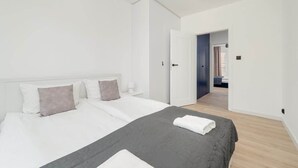 A modern bedroom with a large bed, a bedside table, and a door leading to another room.