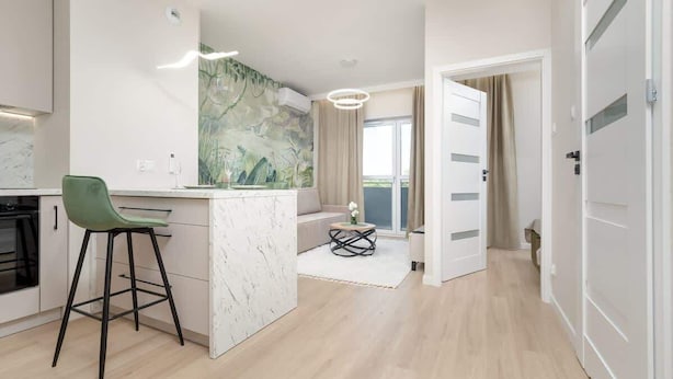 Eine moderne Küche mit einer Marmorinsel, einem grünen Barhocker und einem Essbereich mit einem kleinen Tisch und Stühlen.