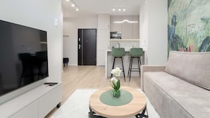 Ein modernes Wohnzimmer mit einem Flachbildfernseher, einem runden Couchtisch mit Blumen und einer Vase, einer Couch und einem Gemälde an der Wand.