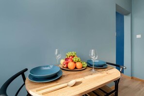 A dining area with a table set for two, featuring a bowl of fresh fruits and wine glasses.