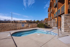 A swimming pool with a stone wall and a metal ladder, surrounded by a fence and a building with balconies. - Studio on Green | Chula Vista, Walk to Attractions (Wisconsin Dells)