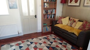 Une pièce avec un tapis à motifs, une bibliothèque, un canapé avec des coussins et une porte.