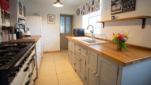 Une cuisine équipée d’une cuisinière, d’un four, d’un évier et d’un four à micro-ondes. On y trouve un plan de travail en bois, un vase avec des fleurs et un tableau noir servant de menu, accroché au mur.