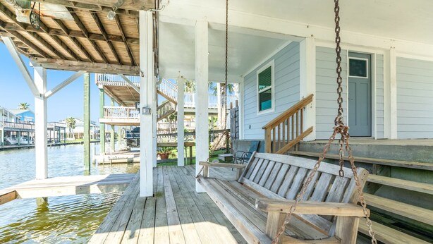 A wooden deck with a swing chair, a covered area, and a view of a water body and buildings in the background.