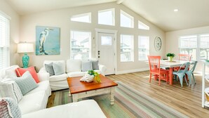 A spacious living room with a white sofa, a wooden coffee table, and a dining area with a white table and orange chairs.