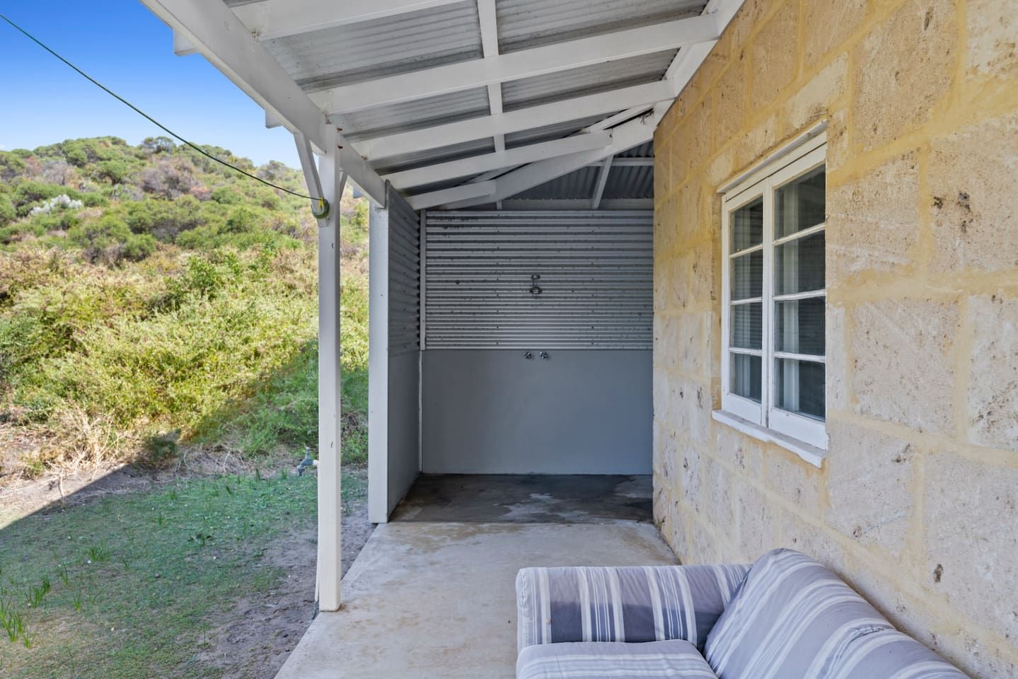 A covered outdoor area with a concrete floor, a white bench, and a garage door.