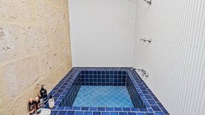 A small bathroom with a blue-tiled bathtub, a shower, and a sink with toiletries.