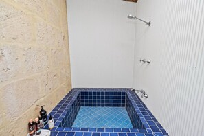 A small bathroom with a blue-tiled bathtub, a shower, and a sink with toiletries.