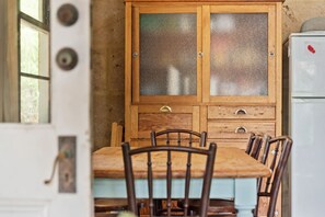 Een houten eettafel met stoelen, een kast met geëtste glazen deuren en een witte koelkast.