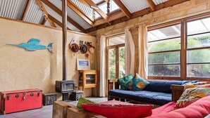 A cozy room with a wooden ceiling, a blue sofa, a red suitcase, and a small TV. - Kangaroo Cottage – Beachside Escape in Dawesville (Dawesville)