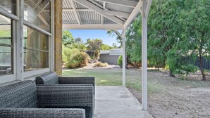A covered patio area with wicker furniture and a concrete pathway leading to a backyard. - Kangaroo Cottage – Beachside Escape in Dawesville (Dawesville)