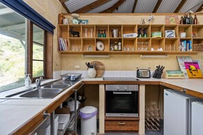 A compact kitchen with a sink, stove, and a shelf above containing various kitchen items.