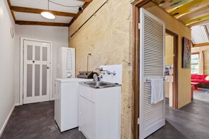 Een wasruimte met een wasmachine, een wasbak en een deur naar een kamer met een rode bank.