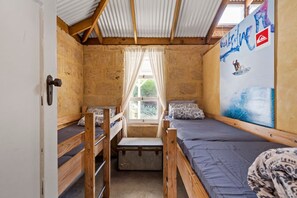 A compact room with bunk beds, a window with curtains, and a wall with a surfing-themed mural.