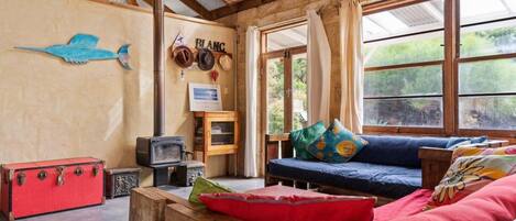 A rustic interior with a wooden ceiling, a blue sofa with colorful cushions, a red suitcase, and a vintage television.
