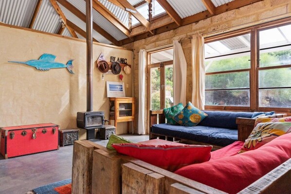 A rustic interior with a wooden ceiling, a blue sofa with colorful cushions, a red suitcase, and a vintage television.