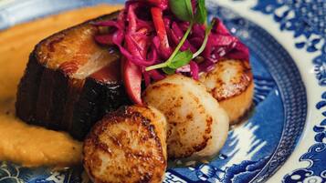 A plate with seared scallops, roasted potatoes, and a beetroot salad on a blue and white patterned plate.