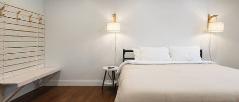 A bedroom with a bed, bedside tables, a wall-mounted shelf, and two wall-mounted lamps.