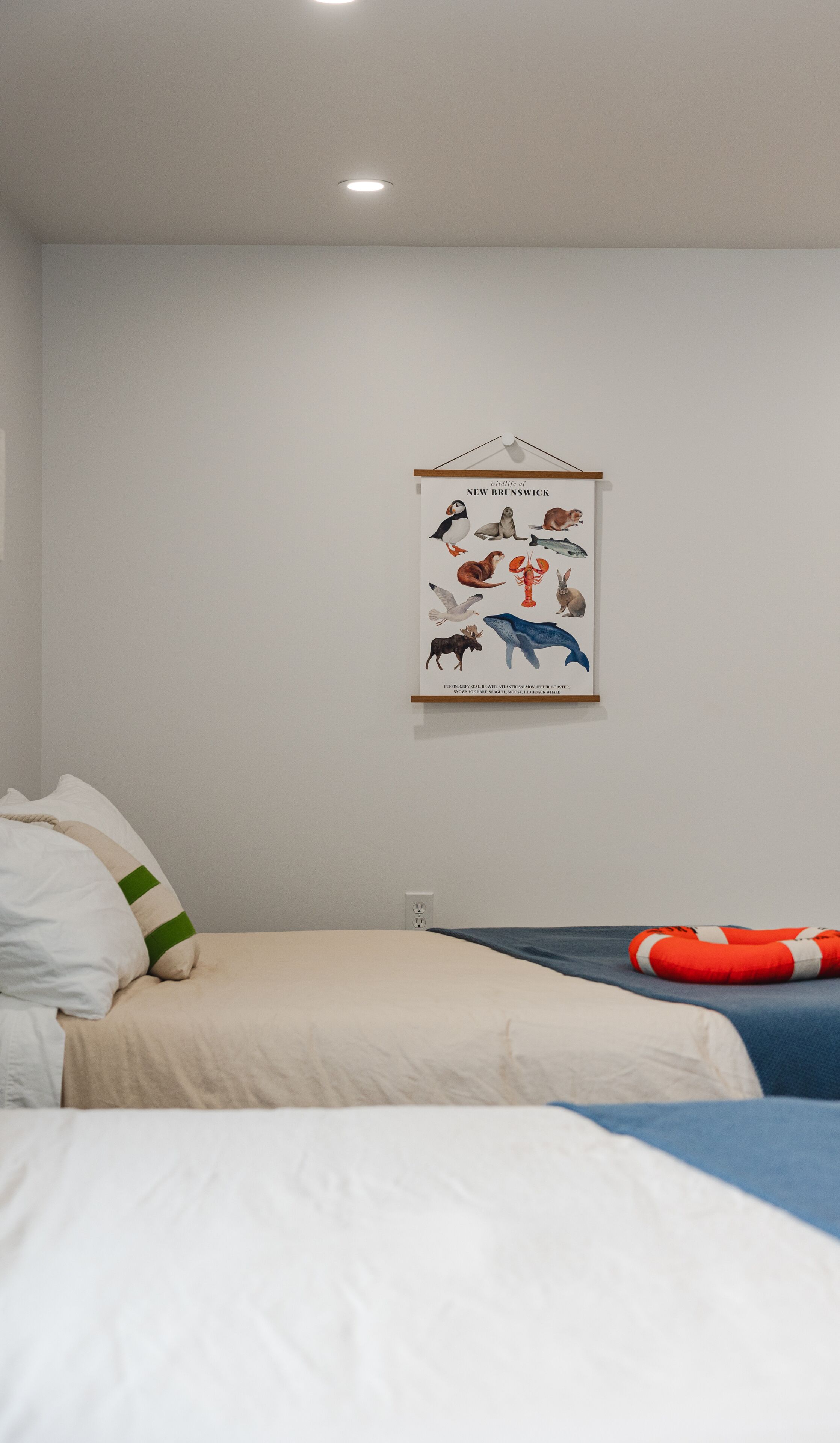 Une chambre à coucher avec un lit, des oreillers, une affiche représentant la faune de la Nouvelle-Brunswick accrochée au mur, et une prise de courant.
