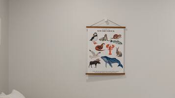Une chambre à coucher avec un lit, des oreillers, une affiche représentant la faune de la Nouvelle-Brunswick accrochée au mur, et une prise de courant.