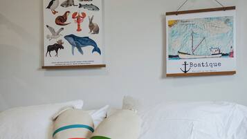 Een bed met witte beddengoed en kleurrijke kussens, een poster van dieren uit New Brunswick, en een kaart van een boot.