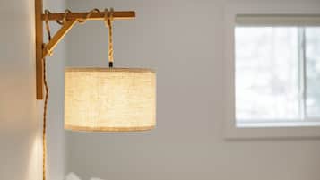 En hänglampa med en lampskärm med mönstrad yta, upphängd i ett rep från en träbalk.