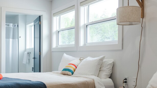 A hotel room with two beds, a window, a lamp, and a door leading to a bathroom. - Homeport Suites & Residences (Lords Cove)
