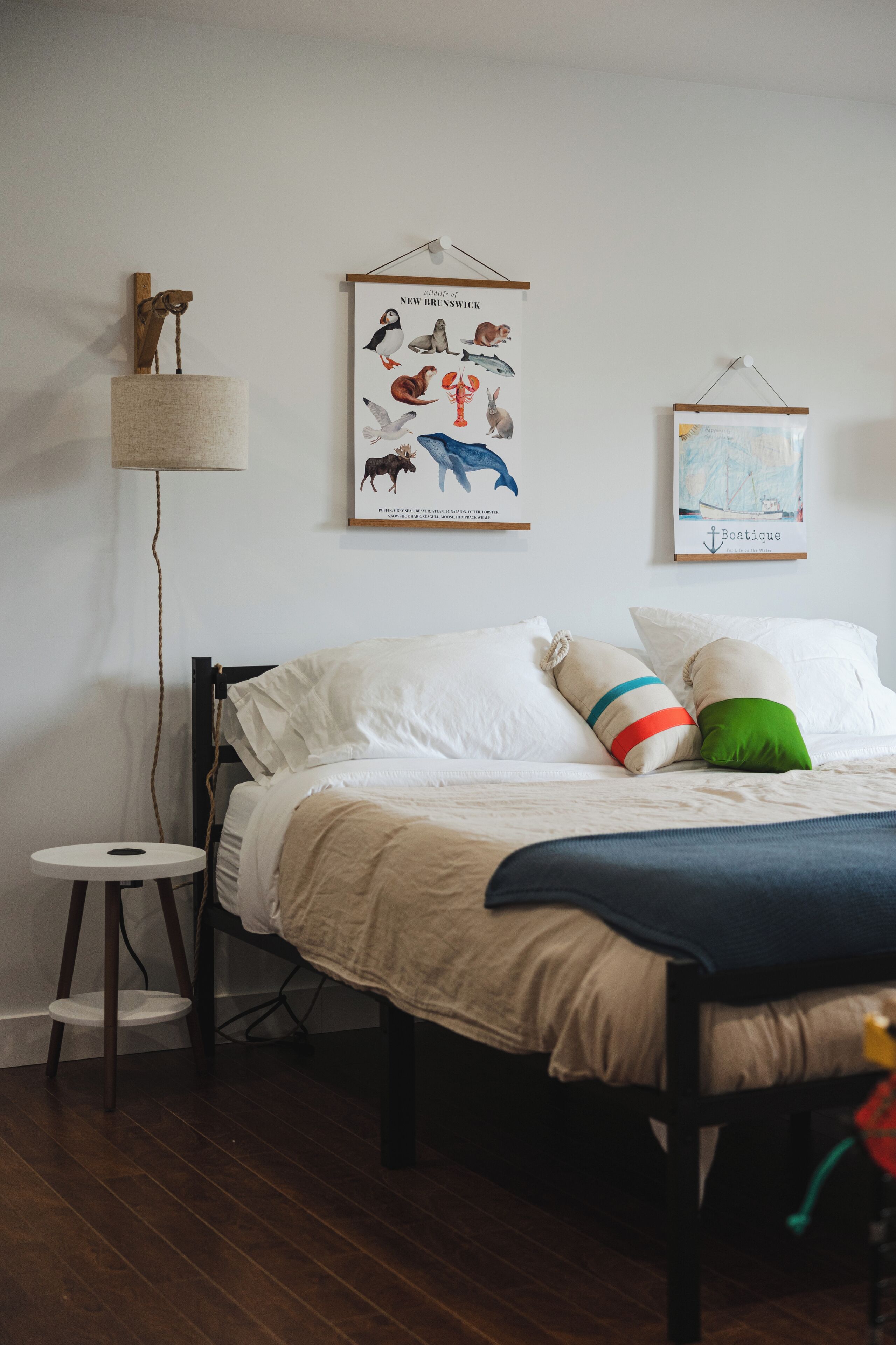 A bedroom with a bed, a small stool, a hanging lamp, and two framed pictures on the wall.