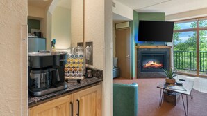 A kitchen with a coffee maker, a Keurig, and a coffee pod dispenser. There is a fireplace with a fire, a television mounted above it, and a view of the outdoors through a large window. - Tee Time Terrace - Near Attractions / Waterpark (Wisconsin Dells)