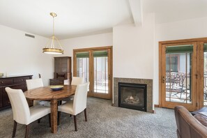 A dining area with a wooden table, white chairs, a chandelier, a cabinet, and a fireplace.