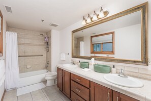 A bathroom with a bathtub, toilet, and sink, featuring a large mirror and a shower area.