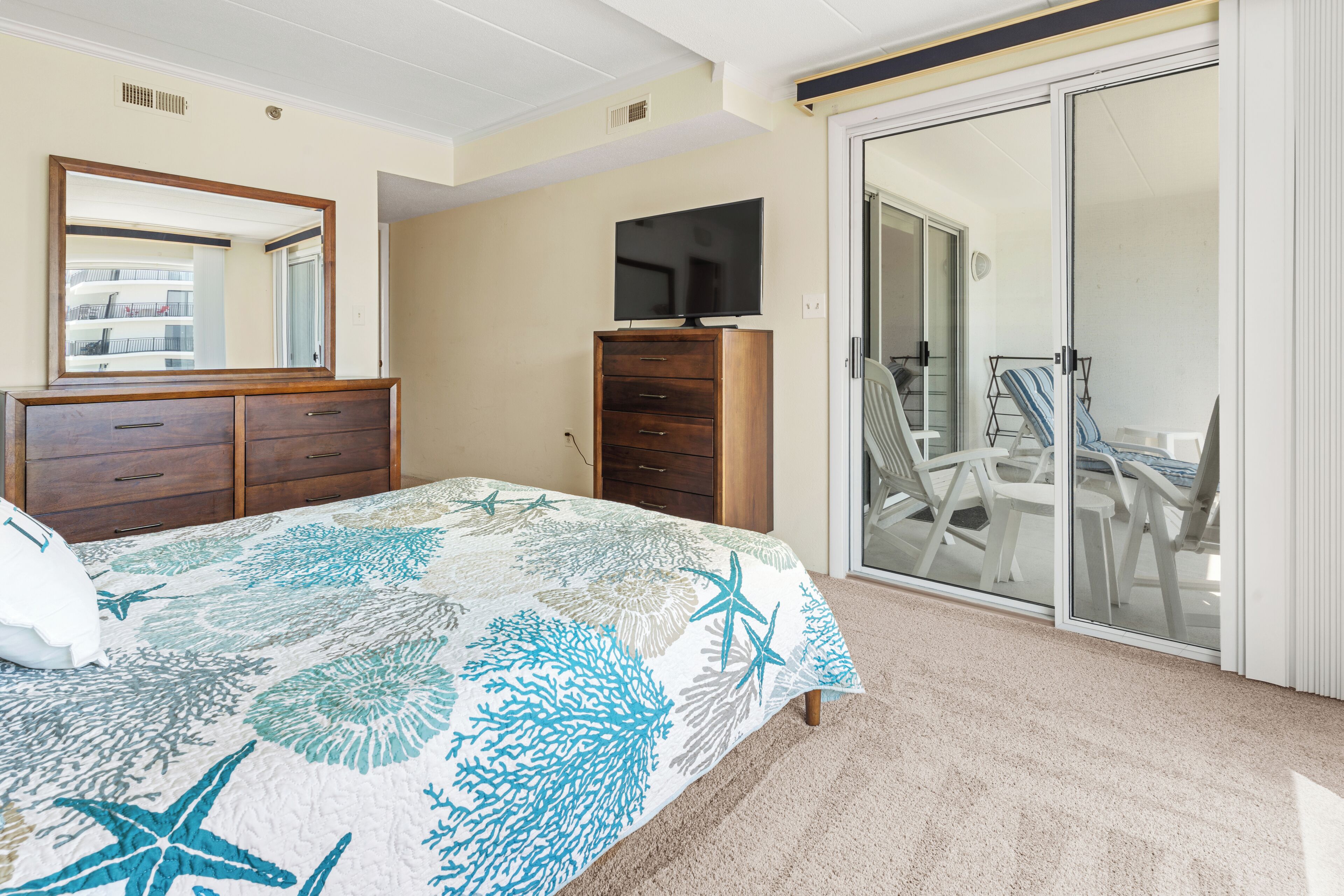 Een slaapkamer met een bed, een dressoir, een televisie en een schuifdeur naar een balkon.