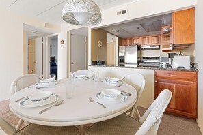 Un coin repas avec une table ronde pour quatre personnes, entourée de chaises, et une cuisine dotée de meubles en bois et d’appareils électroménagers.