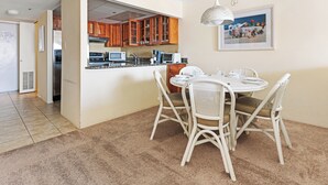 Un coin repas avec une table ronde et des chaises blanches, une cuisine avec des meubles en bois et un tableau accroché au mur.