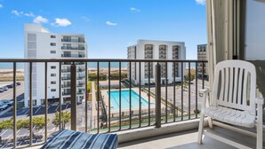 Un balcon donnant sur une piscine, les bâtiments adjacents et un espace de stationnement.