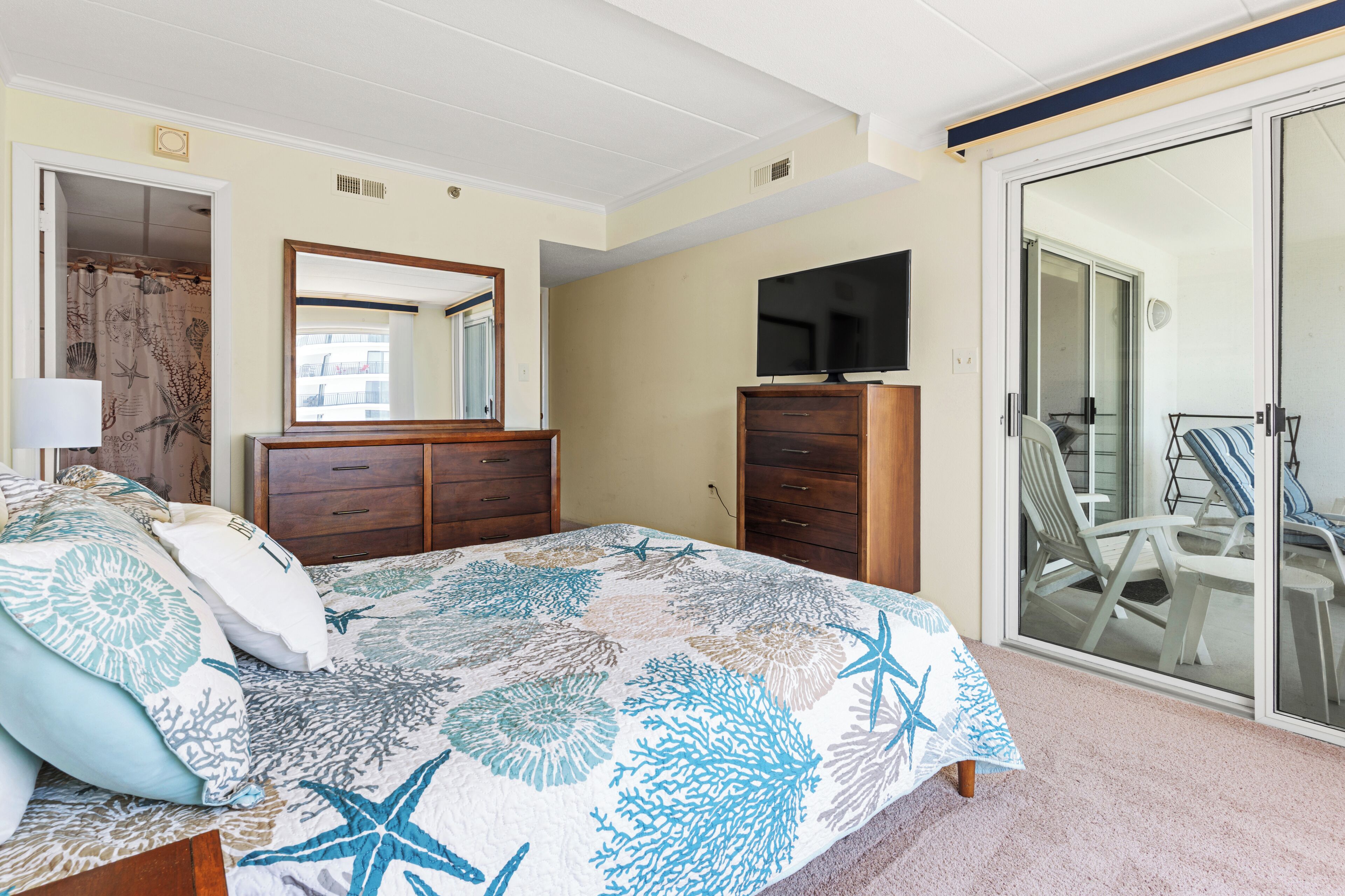 Een slaapkamer met een bed, een dressoir, een televisie en een schuifdeur die leidt naar een balkon.