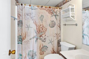 Une salle de bain avec un rideau de douche à motifs nautiques, des toilettes blanches et un lavabo blanc.
