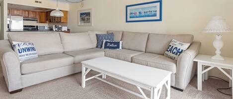 Ein Wohnzimmer mit einem Ecksofa, einem weißen Couchtisch und einer Lampe.