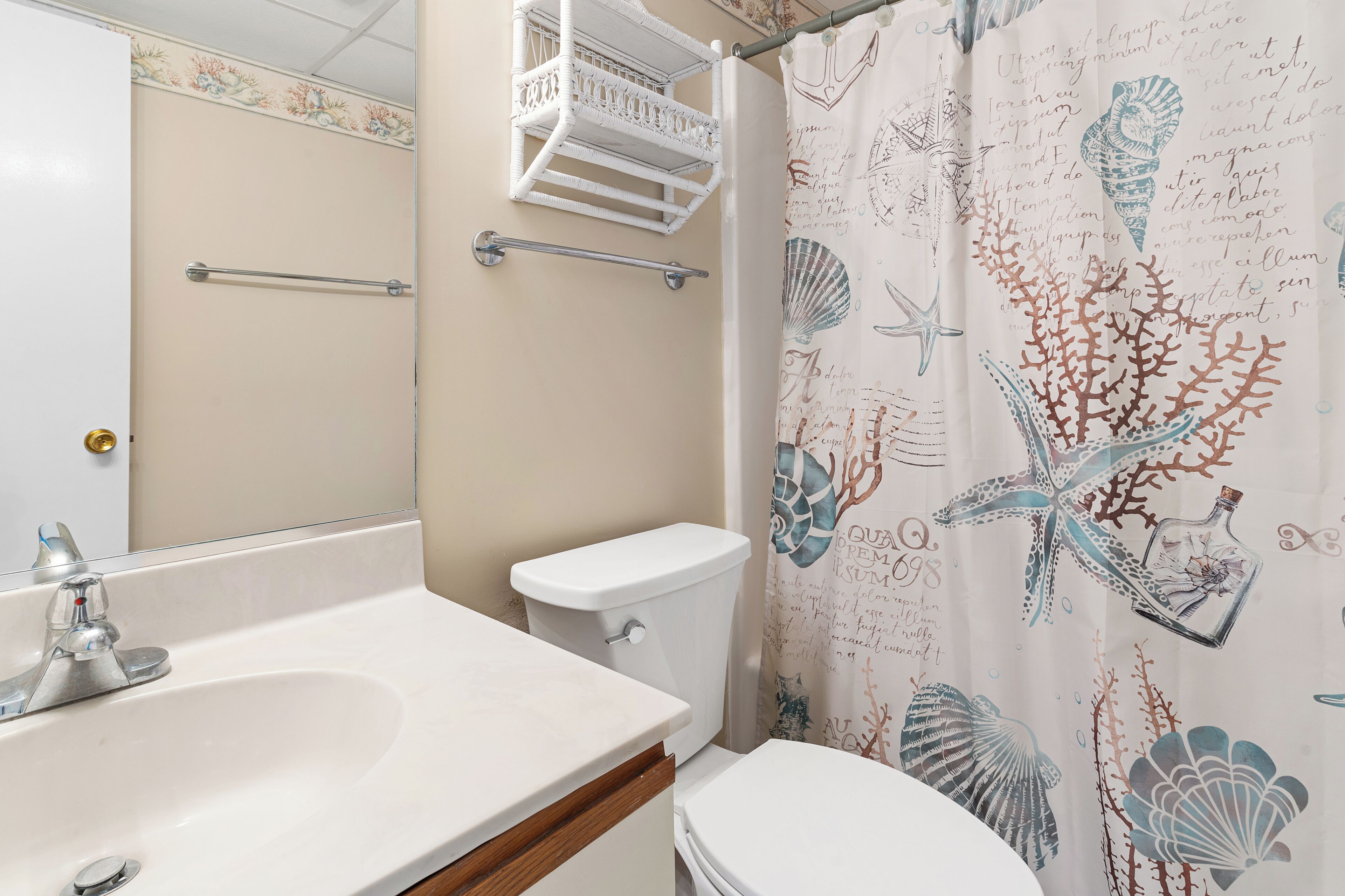 A bathroom with a white sink, toilet, and shower curtain with sea-themed designs.