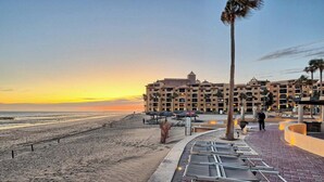 Ein Hotel direkt am Strand mit Poolbereich, Palmen und Blick auf den Sonnenuntergang über dem Meer.