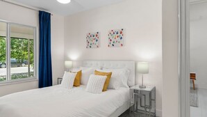 A modern bedroom with a large bed, two bedside lamps, a ceiling fan, and two wall art pieces. - Uhost AI 1B Retreat Fully Equipped w Patio (Fort Lauderdale)