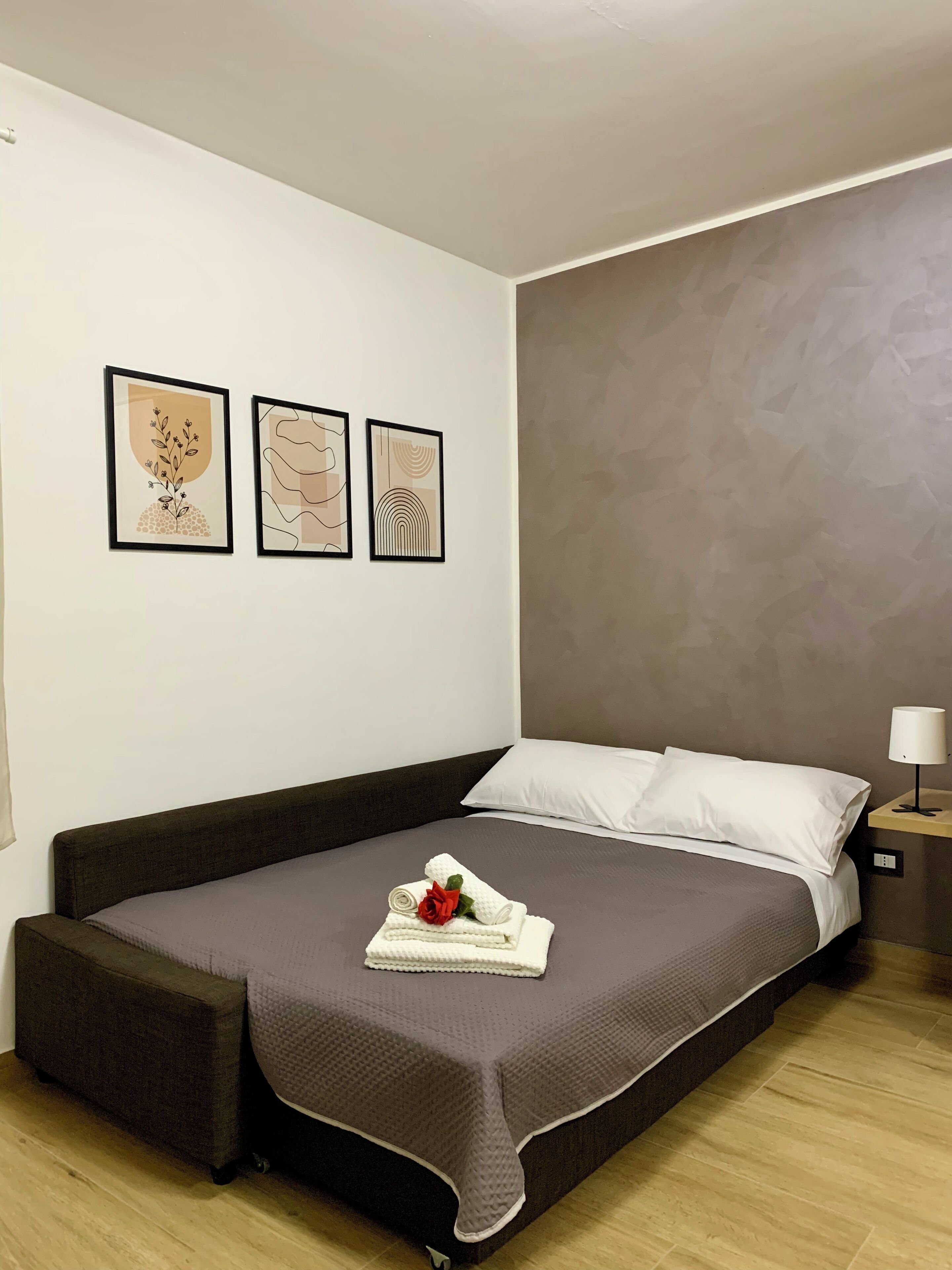 Ein modernes Schlafzimmer mit einem Bett, einem Nachttisch und drei gerahmten Kunstwerken an der Wand.